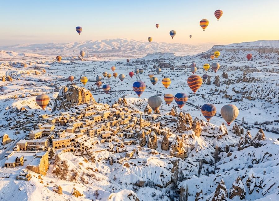 Hot air balloon flying over snowy Cappadocia during winter sunrise