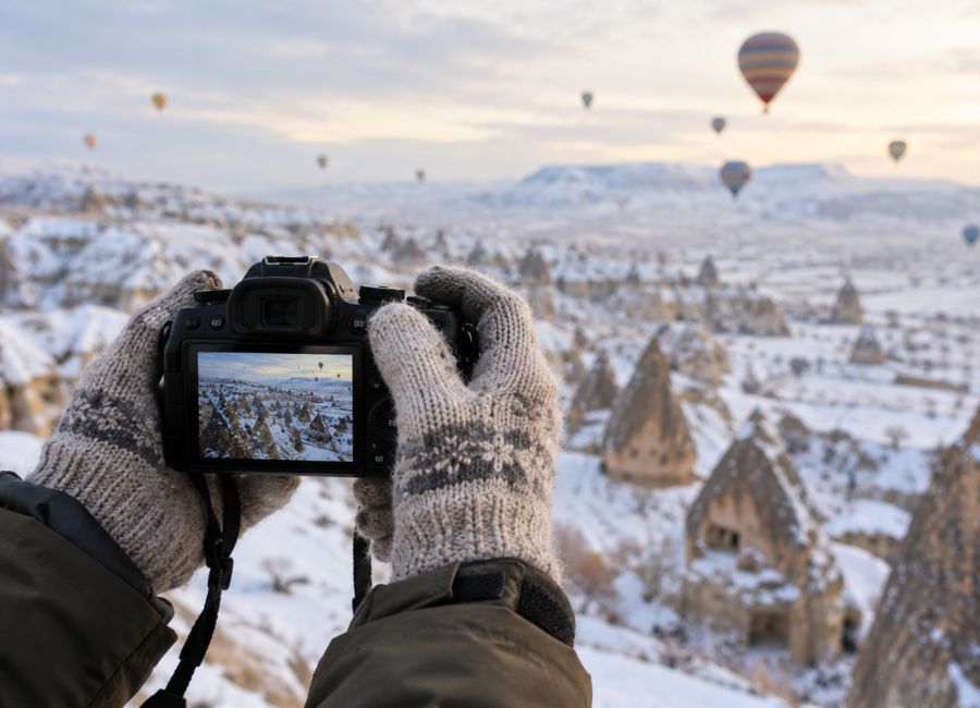 Gloved hands holding a camera at a snowy Cappadocia viewpoint
